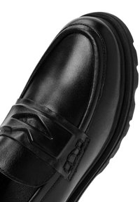 Mocassin en cuir noir avec une bande texturée et des coutures délicates. Bout arrondi, semelle en caoutchouc épaisse et design épuré et minimaliste.