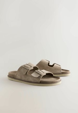 Sandali beige in camoscio con due fibbie regolabili, design con punta aperta e suola testurizzata, caratterizzati da un bordo cucito e un dettaglio ritagliato.