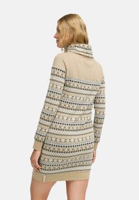 Robe en tricot avec un col drapé, présentant une base beige avec des accents à motifs en noir et crème. Manches longues et poignets côtelés.