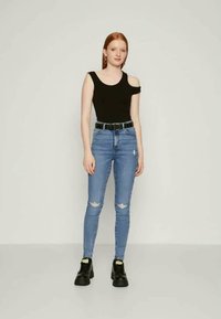 Top negro de un solo hombro, jeans ajustados azules con rodillas rasgadas y zapatos gruesos negros. Diseño sencillo, forma ajustada, textura suave.