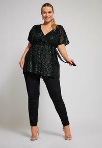 Top avvolgente nero con paillettes, scollatura a V, maniche corte e cintura regolabile, abbinato a pantaloni neri aderenti e tacchi trasparenti con lacci.