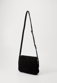 Mustmust värvi rihmaga crossbody kott pikema reguleeritava rihmaga, ristküliku kuju ja ühe esipocketiga. Sile tekstuur ja minimaalne riistvara.