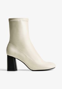 Botine bej până la gleznă, realizate din material sintetic neted, cu un toc gros negru cu o textură în dungi verticale. Design elegant și ajustat.