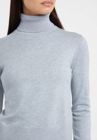 Maglione a collo alto azzurro chiaro in morbido jersey a costine. Presenta un design aderente con il logo ricamato "GUESS JEANS" sul petto.