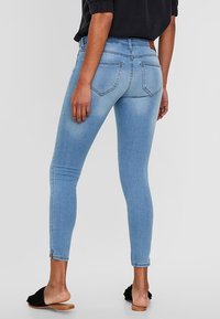 Jeans skinny de mezclilla azul claro con un diseño de cintura alta, que cuentan con bolsillos traseros y un ligero desvanecimiento. Combinados con sandalias planas color tostado.