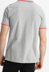 Polo shirt gris à manches courtes avec des accents côtelés rouges au col et aux manches, présentant une coupe décontractée et une texture douce.