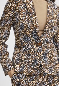 Blazer mit taillierter Passform, ausgestattet mit einem mehrfarbigen Punkte-Muster in Braun, Creme und Blautönen; einzelner Knopfverschluss und spitze Revers.