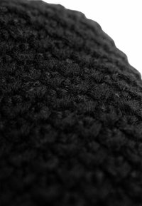 Black textured fabric with a woven pattern, featuring dense, plush surface details that create a soft appearance.