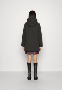 Dark green, hooded jacket with a relaxed fit. Features a smooth texture and minimal detailing. Paired with a plaid skirt and knee-high black boots.