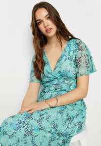 Une robe à motifs léopard turquoise avec de courtes manches flottantes et un décolleté en V, présentant une texture froncée et un tissu lisse.