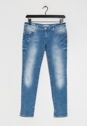 Jean skinny en denim bleu avec des détails délavés et des plis, suspendu à un cintre noir sur fond blanc.
