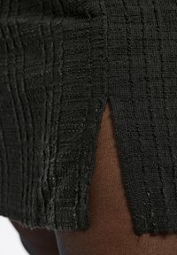 Svart texturerad tyg med ett vertikalt randmönster, med en framspringa som avslöjar brunt material under.