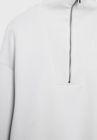 Pull-over gris clair avec un col montant, doté d'une fermeture éclair à moitié sur le devant, d'un col côtelé et d'un panneau texturé sur la poitrine.