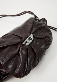Dark brown leather clutch purse with a ruched design and silver rectangular clasp, featuring a thin leather strap on a white background.