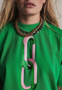 Sudadera verde con un gran gráfico de un diseño de clip de papel en rosa y verde. Cuenta con un cuello redondo y mangas cortas, textura suave.
