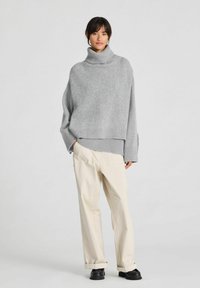 Hall hallatud kampsun kõrge kaelusega, soonikkoes varrukate ja äärega. Kombineeritud kreemja laia säärega pükste ja mustade kingadega.