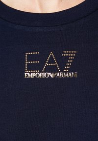 Marinblå t-shirt med ett guldnitat "EA7 Emporio Armani"-logotyp på bröstet, rund halsringning och slät tygtextur.