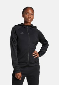 Felpa nera con zip realizzata in tessuto liscio, dal design aderente. Presenta un cappuccio, tasche laterali e un logo discreto sul petto.