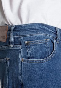 Blauwe spijkerbroek van denim met een klassieke pasvorm, voorzien van een leren label in de taille, koperen hardware accenten en subtiele vervagingen in de stof.