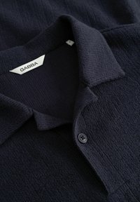 Maglia a coste di colore blu navy scuro con colletto, chiusura con bottoni e etichetta del marchio bianca visibile con la scritta "GABBA" all'interno del collo.