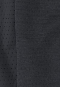 Grauer Strickstoff mit zwei Texturen: eine glatt und einfarbig, die andere mit kleinen, erhabenen schwarzen Punkten in einem Rastermuster.