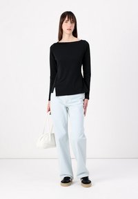 Black long-sleeve top with a square neckline, paired with light blue wide-leg jeans and black shoes. Holds a white handbag.