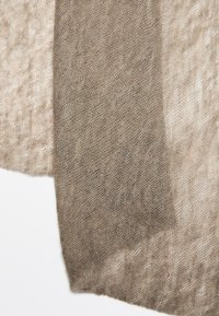 Lekki, przezroczysty szal w odcieniach beżu i taupe, z teksturowanym, tkanym wzorem o subtelnych różnicach kolorystycznych. Krawędzie są delikatnie wykończone.