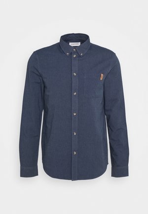 Chemise boutonnière bleu foncé en tissu denim, avec une poche avant, un col boutonné et des boutons marron clair.