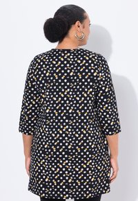 Tunica nera con un motivo a pois in bianco e giallo. Presenta maniche a tre quarti, una vestibilità comoda e una texture del tessuto liscia.