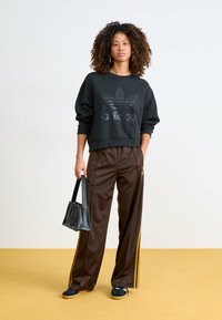 Fekete pulóver textúrált logóval, barna selyem sportnadrág sárga oldalsávokkal és egy kis fekete kézitáska. Alacsony profilú sportcipők.