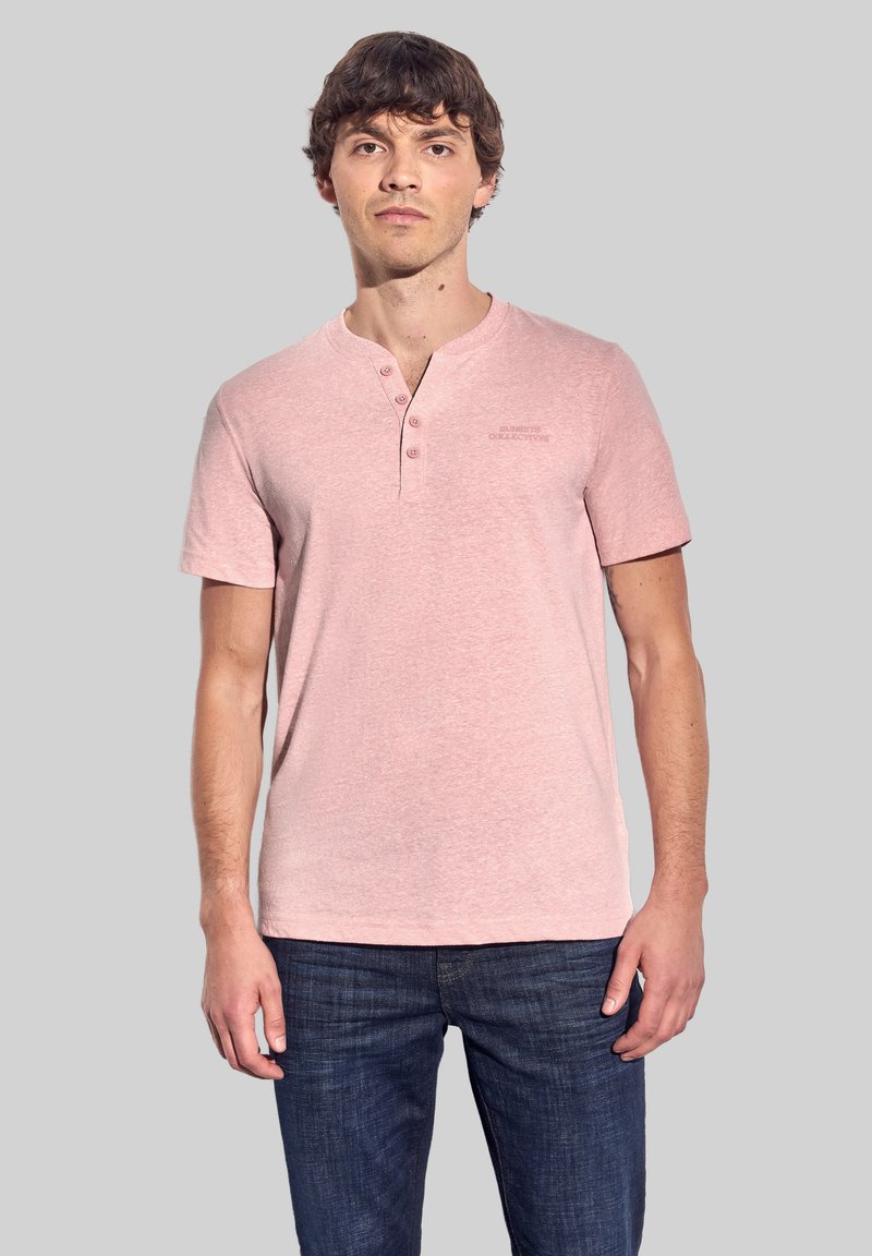 Světle růžové tričko s výstřihem do V, krátkým rukávem, třemi knoflíky a jemnou strukturou, spárované s tmavě modrými džíny.