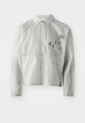 Veste coupe-vent gris clair en matériau léger, dotée d'une fermeture éclair à l'avant, d'un col et de textes et graphiques imprimés dans des tons atténués.