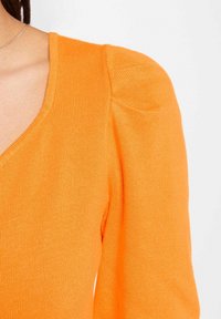 Haut en maille côtelée orange avec un col en V et des manches bouffantes. La texture semble lisse ; il présente une coupe ajustée et un design structuré des manches.