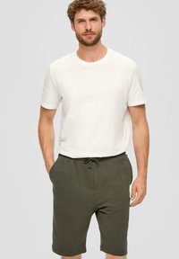 Weißes Baumwoll-T-Shirt mit kurzen Ärmeln, kombiniert mit olivgrünen Sweat-Shorts. Die Shorts verfügen über einen elastischen Bund mit Kordelzug und seitliche Taschen.