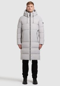 Hellgraue Daunenjacke mit langer Silhouette, verstellbarem Kapuzen, Front-Reißverschluss, großen Taschen und schwarzen Akzenten. Verfügt über gepolsterte Nähte.