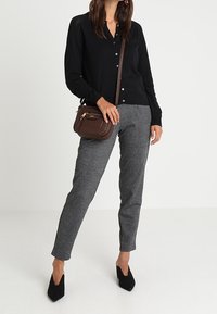 Musta neulottu neuletakki, jossa napit, harmaat kuvioidut räätälöidyt housut ja pieni ruskea olkalaukku. Asun täydentävät mustat teräväkärkiset korkokengät.