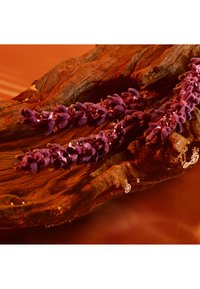 Rami di lavanda viola con gocce d’acqua appoggiate su legno marrone testurizzato su uno sfondo arancione caldo.