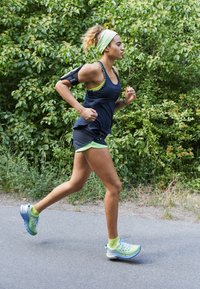 Tenue de sport comprenant un débardeur foncé, des accents verts et un short noir. Chaussures de course vert clair avec une semelle texturée. Course dans un cadre naturel.