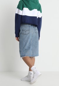 Cropad, färgblockerad hoodie i grön, vit och marinblå som kombineras med en ljusblå denimkjol med fransar, bärs med vita sneakers.