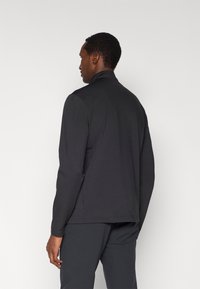 Jachetă neagră cu mâneci lungi, guler înalt, textură netedă și croială ajustată. Dispune de un tiv drept și un stil minimalist.