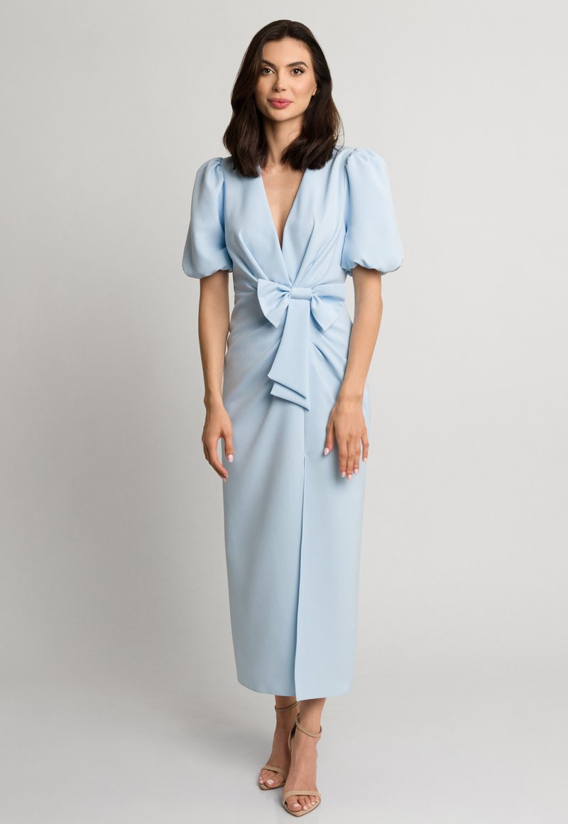 Jasnoniebieska, do kolan sukienka z dekoltem w serek, bufiastymi rękawami i detalem w postaci kokardy z przodu. Wykonana z gładkiego materiału o dopasowanym kroju.