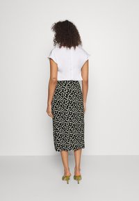 Weißes Kurzarmoberteil kombiniert mit einem schwarzen Midirock mit weißem Blumenmuster. Grüne Absatzsandalen vervollständigen das Outfit.