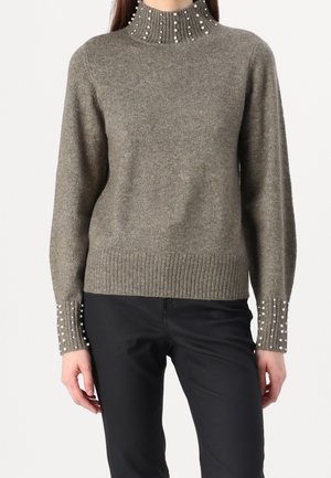 Woman wearing gray knit sweater with high ribbed collar and cuffs adorned with rows of small white pearls, paired with black pants.