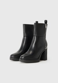 Bottines en cuir noir avec une finition lisse, talon carré, zip latéral et ouvrez-onglets ; la semelle texturée offre une bonne traction.