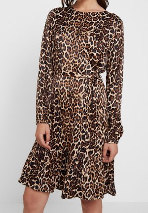 Vrouw draagt een jurk met lange mouwen, knielengte, met een luipaardprint en een gerimpelde zoom.