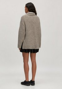 Übergrößen, hellbrauner Strickpullover mit breitem Kragen und gerippten Kanten, getragen über einem schwarzen, frilly Rock, von hinten gezeigt.