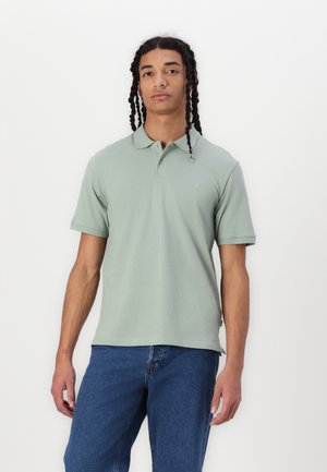 Polo verde claro com colarinho e três botões, feito de algodão macio, combinado com jeans azul.