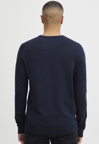 Suéter de punto azul marino, cuello redondo, mangas largas, puños y bajo acanalados, textura suave, diseño ajustado sin patrones visibles ni herrajes.