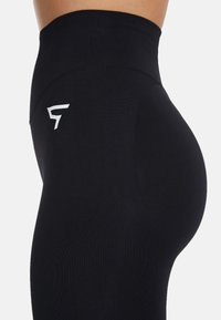 Hoge taille zwarte leggings van rekbaar materiaal, met een gladde textuur, een strakke pasvorm en een wit logo aan de zijkant.