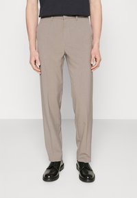 Béžové kalhoty na míru s hladkou texturou, rovného střihu a s poutky na pásek. Kombinovány s černými koženými botami.